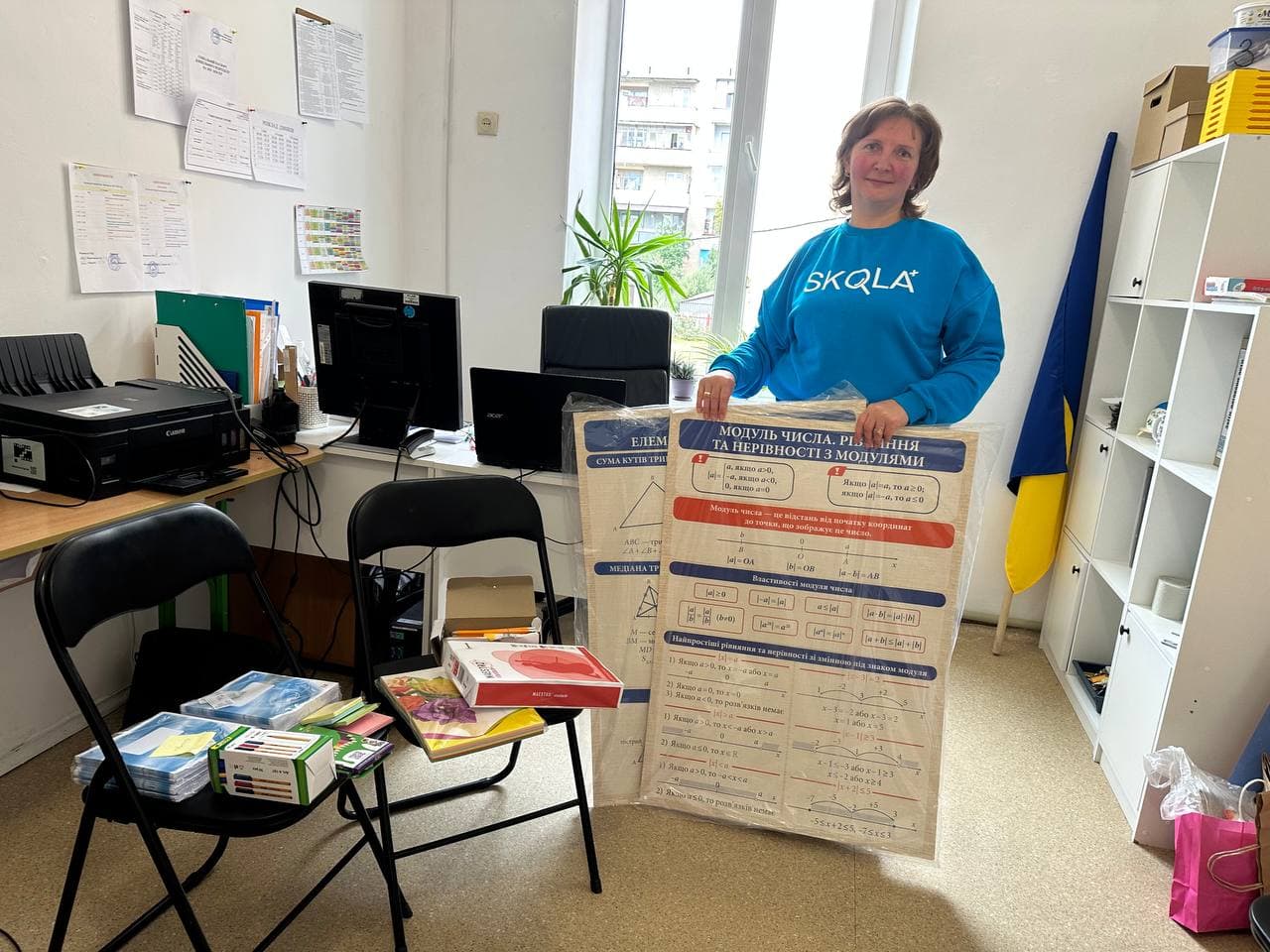 SKOLKA teacher holding a new mathematics teaching poster in her office with textbooks and supplies