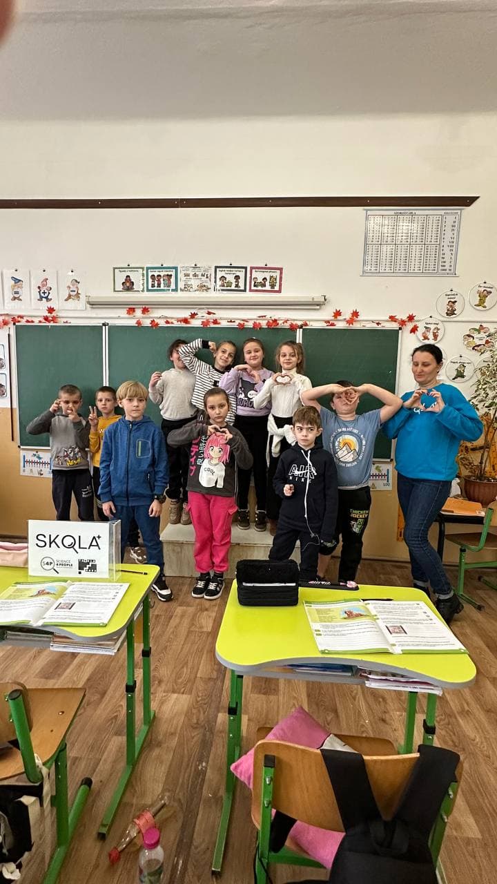Schoolchildren making heart gestures with their hands alongside their SKOLKA teacher in a classroom